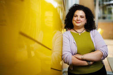 Christina Delimitrou leans against a yellow wall outside of Stata Center.