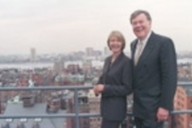 Lore Harp McGovern and Patrick McGovern Jr. at IDG's Boston headquarters, with the Cambridge and MIT skyline in the background.