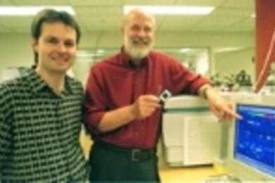 Professor Richard O. Hynes, director of the Center for Cancer Research, holds a glass slide containing thousands of bits of DNA that have been exposed to genetic material from tumor cells. He and former postdoctoral fellow Edwin A. Clark (left), now at Millennium Predictive Medicine in Cambridge, collaborated with other scientists to identify the gene responsible for cancer metastasis.