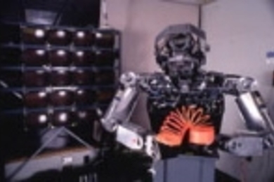 This picture of Cog, a humanoid robot created by a team of researchers at the AI Lab led by Professor Rodney Brooks, was taken in March 1998. Cog is playing with a Slinky toy; the bank of computers to his right is linked to his vision. See related story on Humanoid2000 conference.