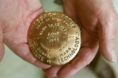 A closeup of the brass benchmark (in alumnus Philip Simmons' hands)        that he placed on a bridge road in Maine in 1948.