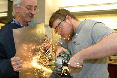Professor Woodie Flowers of mechanical engineering helps senior John Rebula work on part of a manioc grater, designed to grate large quantities of manioc or kasava for food in Haiti. The project is for 2.009, whose final presentations are Monday, Dec. 12.