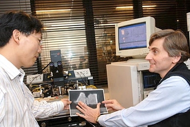 Postdoctoral associate Dae-Hyun Kim, left, and Professor JesÃºs del Alamo look at a cross-section of the new transistor they have been developing. Behind them is the test equipment used to measure its characteristics.