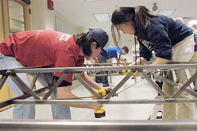 Members of MIT's regional Steel Bridge Competition team replicated their high-speed construction at a department celebration of their victory. Shown in the photo are junior Tracy Takemura, right, and sophomore Jose Cano, left. Quinn Vollmert, a junior, is in blue T-shirt at back.