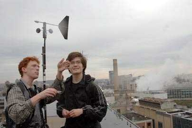 Fourth-year Ph.D. student in materials science Dan Wesolowski, left, discusses wind direction and velocity on a rooftop with mechanical engineering sophomore Richard Bates. They and other students put equipment on a number of roofs around the Institute for a month to determine the viability of using wind turbines to generate power. MIT's co-generation plant is visible behind them.
