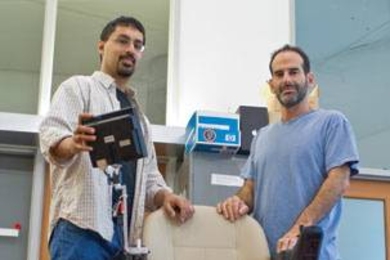 Nicholas Roy, left, assistant professor of aeronautics and astronautics, and Seth Teller, professor of computer science and engineering, stand next to the robotic wheelchair they co-designed, which can be navigated by vocal command.