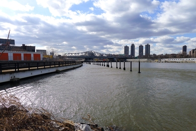 A Bronx-side view of the waterfront's existing conditions, featuring natural edge conditions, elements of the industrial working waterfront, the freight railroad, storage facilities, and the 3rd Avenue Bridge spanning the Harlem River.