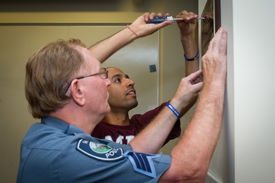 MIT Police Sergeant Richard Sullivan (foreground) and Anirban Mazumdar hang the plaque they made to honor Officer Sean Collier in the MechE Student Commons. 