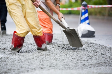 Two people are ankle-deep in cement while holding shovels pointed downwards.