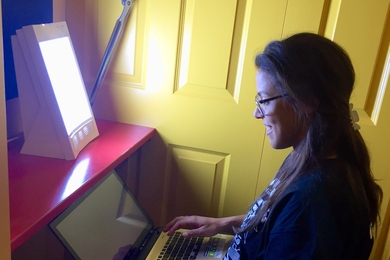 A fourth-year PhD student in electrical engineering and computer science, Ariel Anders works beside a light-therapy box recently installed at MIT.