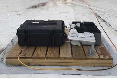 The team’s test device, which has been deployed on the roof of an MIT building for several months, was used to prove the principle behind their new energy-harvesting concept. The test device is the black box at right, behind a weather-monitoring system (white) and a set of test equipment to monitor the device’s performance (larger black case at left).
