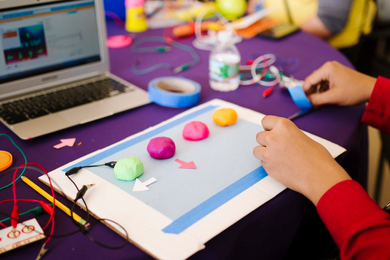 A child's hands work with putty balls, some of which have electrodes sticking out of them