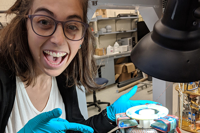 Photo of Chiara Salemi with blue latex gloves pointing at the ABRACADABRA toroid magnet