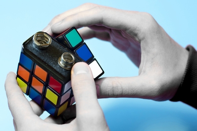 Conceptual photo featuring two hands, each turning a section of a battery that looks like a Rubick's cube