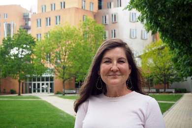 Photo of Laurie Boyer standing in front of trees and MIT's Stata Center, a building with a half-brick, half-metal facade