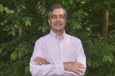 Photo of Abhay Ram from waist up with arms crossed in front of greenery
