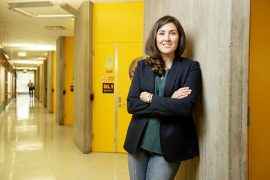 Photo of Katie Galloway standing in a colorful hallway, with arms folded and smiling at the camera