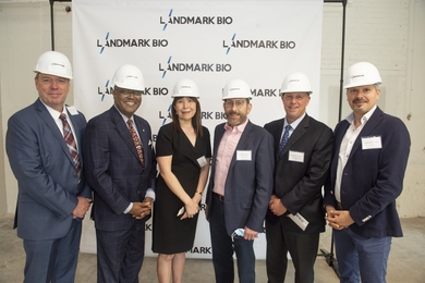 Posed shot of six individuals wearing suits and construction hard hats in front of a banner printed with "LandmarkBio"