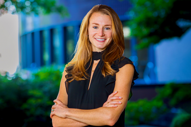 Portrait photo of Kristin Knouse, standing with her arms folded against a blurred outdoor background