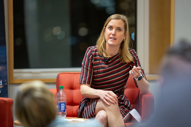 Photo of Poppy Allonby sitting in red chair and speaking to a crowd. 