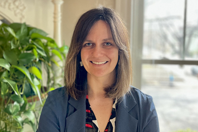Portrait photo of Paige Bollen seated next to a houseplant and a window