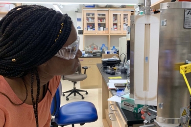 Photo of an MIT undergraduate student looking at a tabletop machine inside an engineering lab