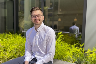 Photo of Evan Leppink sitting in front of bright green grasses on MIT campus