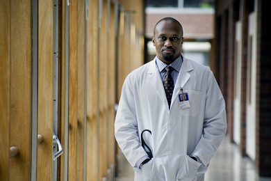 Photo of Collin Stultz standing in a hallway, wearing a white physician's coat