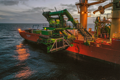 A large orange and green ship lowers the much smaller green Patania II vessel into the ocean.