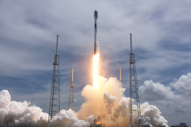 The SpaceX Falcon 9 rocket launching from the ground against a partly cloudy daytime sky