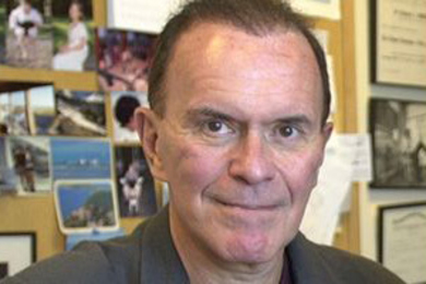 Photo of Richard Wurtman with a sheet of paper in his hand and a bulletin board filled with photos and other memoribilia behind him