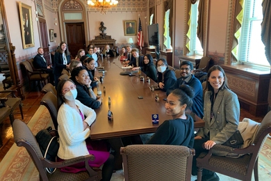 MIT and UDC students and representatives from the US Digital Service sit around a long conference table in an ornate, formal room in the Eisenhower Executive Office Building.