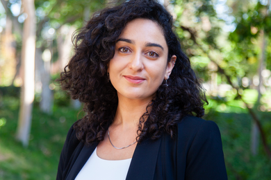 Photo of a woman wearing a dark blazer and standing before a background of out-of-focus trees