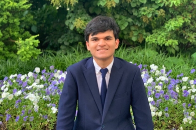 Malhaar Agrawal poses in front of a flower bed, with foliage in the background