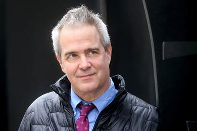 Per Urlaub, wearing a necktie and an insulated jacket open at the collar, looks at something outside of the frame