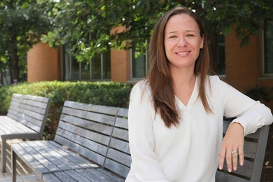 Sara Prescott sitting on an outdoor bench in front of some trees on a sunny day