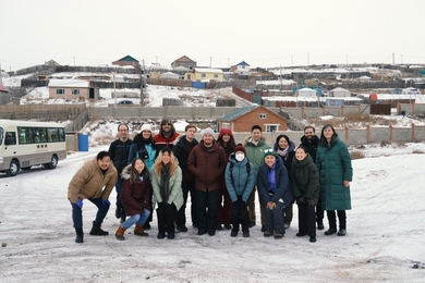 15 students and faculty pose for a group photo in front of snow-dusted residential gers