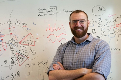 Brandon "Brady" Weissbourd stands in front of whiteboard covered in diagrams and symbols. 