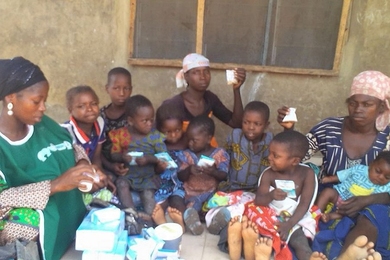 Photo of a dozen individuals, mostly children plus three women, sitting in a group.