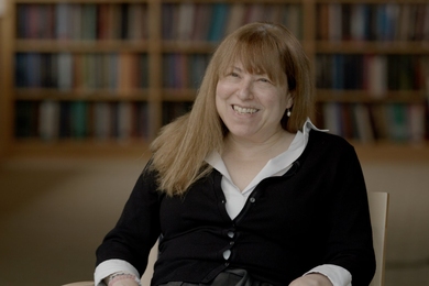 Elly Nedivi smiles as she sits in a chair in a library