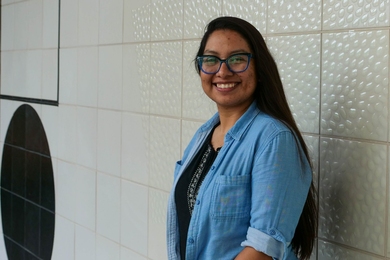 Juana De La O posing in 3/4 profile against a tile wall