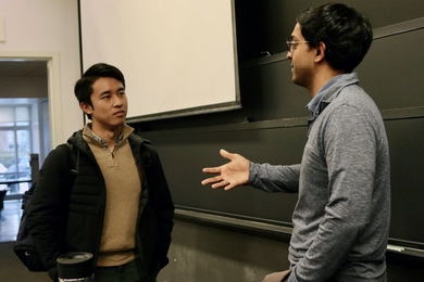 Ashesh Rambachan converses with a student in the front of a classroom.
