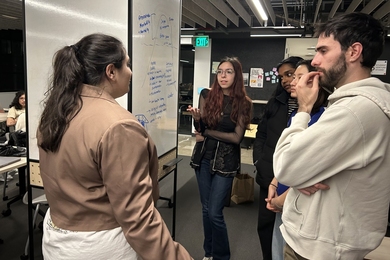 Five students converse around a whiteboard.