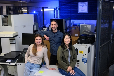 Anastasia Dunca, Chris Rabe, and Jasmin Liu stand in an electronic waste collection area, surrounded by electronic and lab equipment