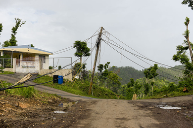 Down power lines at the center of a dirt road with partial view of a house in the upper left corner.
