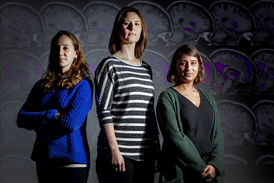 Halie Olson, Kristina Johnson, and Anila D’Mello pose for photo with projected images of MRI brain scans in background