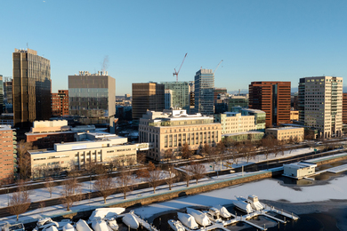 Snowy aerial view of MIT buildings including MIT Sloan, Memorial Drive, and icy river.