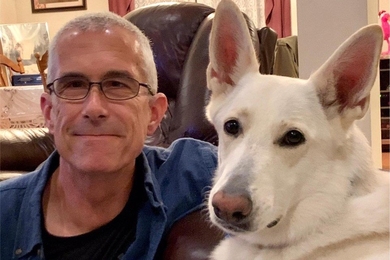 Matthew Dolan sits on a couch with a large white German Shepherd dog