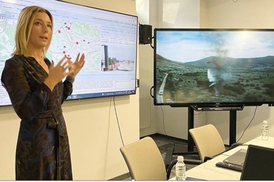 Mirnesa Softić speaks in front of two screens displaying a map and wildfire. 