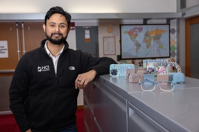 Faraz Faruqi stands next to colorful and texturized objects created by TactStyle, including eyeglass frames, a phone case, a pot, and picture frame.